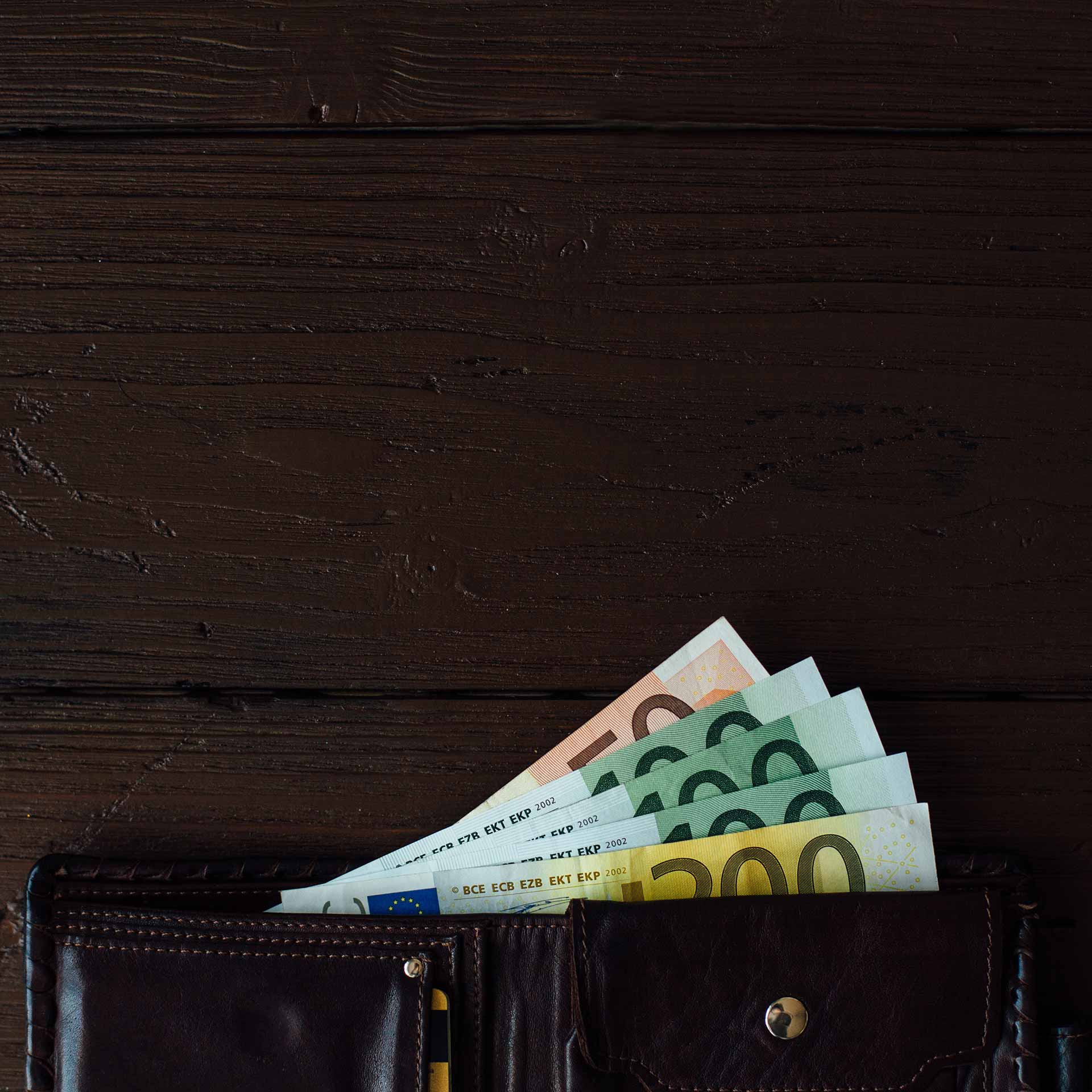 Lederbörse mit mehreren Euro-Geldscheinen auf dunklem Holztisch